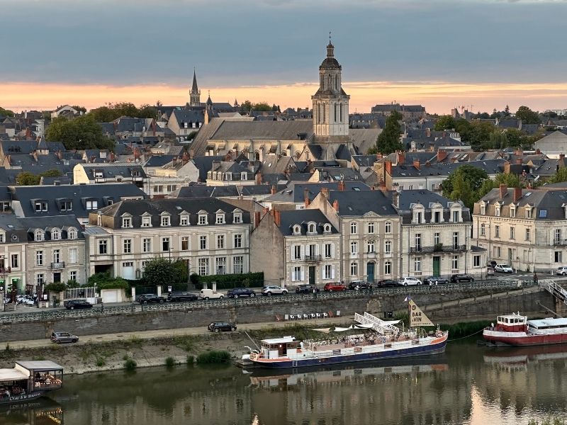 Vista externa das imponentes torres cilíndricas listradas de pedra escura e clara do Castelo de Angers, com um fosso transformado em jardim gramado em primeiro plano, que inspiraram os filmes das princesas da Disney