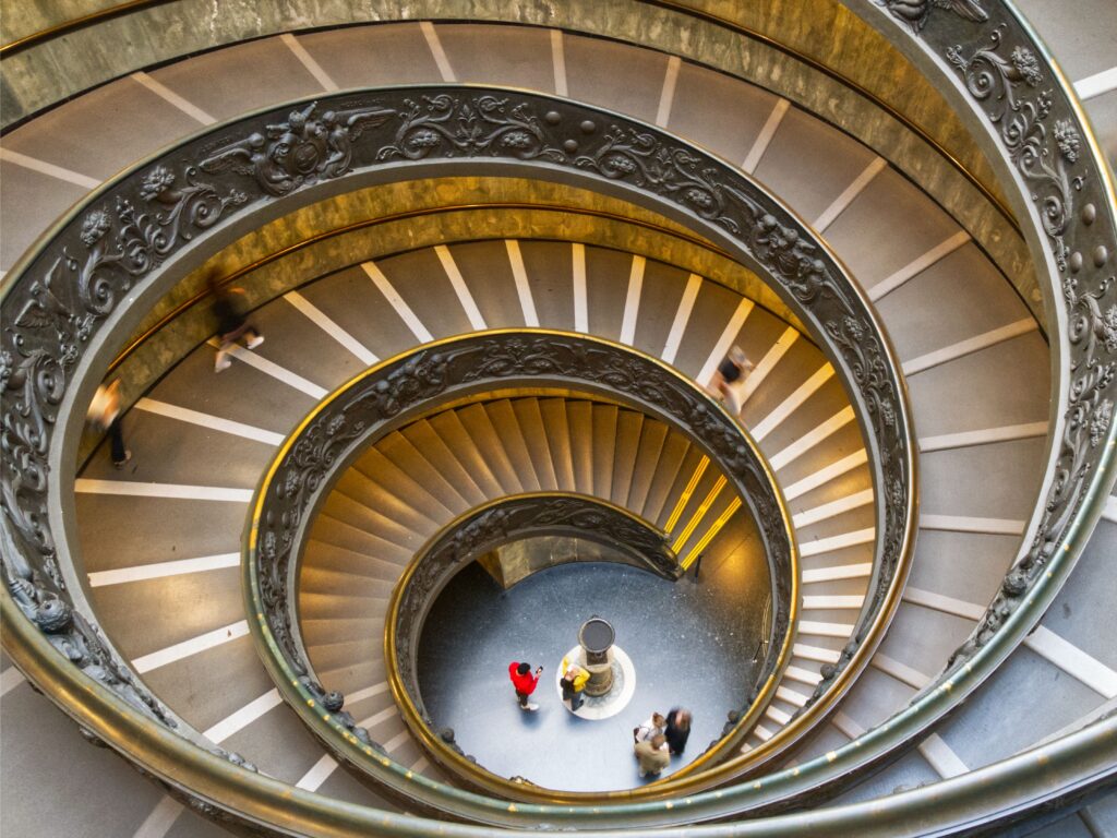 Vista aérea da escadaria helicoidal de Bramante nos Museus do Vaticano em Roma, com visitantes descendo em espiral